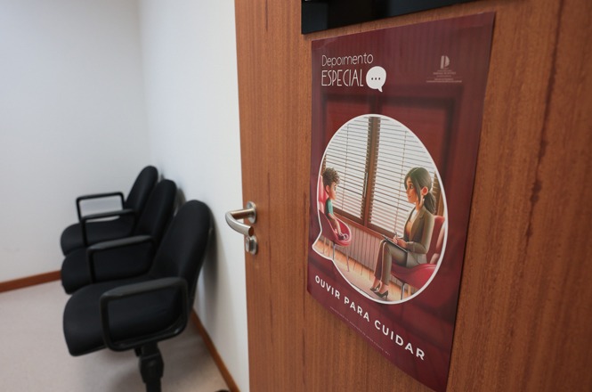 Foto colorida: cartaz “Depoimento Especial” na porta, sala de escuta protegida, atendimento institucional, orientando cuidado em marrom, branco e vermelho
