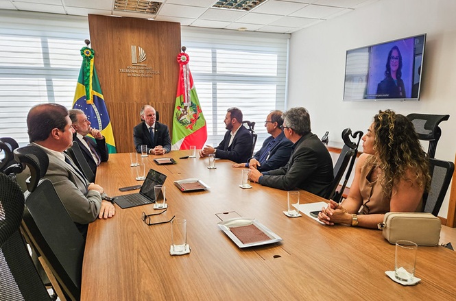 Foto horizontal: O desembargador Rubens Schulz, está ao centro da mesa, entre as bandeiras do Brasil e de Santa Catarina, preside reunião de doação de notebooks