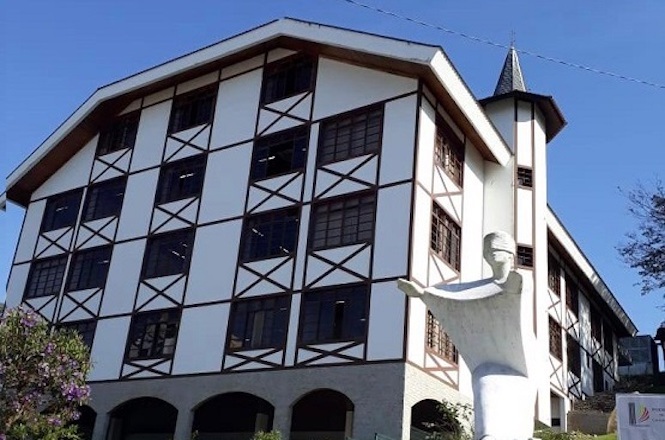 Foto colorida: prédio do fórum com escultura à frente, paisagem urbana externa, sede judiciária, destacando fachada em branco, marrom e azul