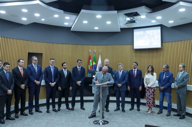 Foto colorida: autoridades alinhadas em plenário institucional, ambiente interno solene, acordo consensual, desembargador do TJSC assinando documento em azul, cinza e verde