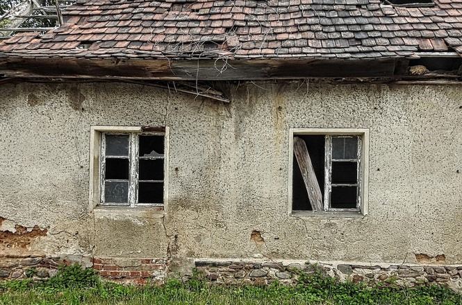 Foto horizontal: casa antiga deteriorada, janelas quebradas e telhado danificado; fachada desgastada