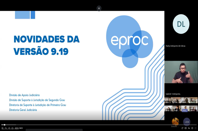 Foto horizontal: slide “Novidades da versão 9.19 eproc” em webinar, com intérprete de Libras na tela