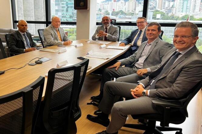 Foto horizontal: desembargador André Luiz Dacol ao centro em reunião com magistrados; mesa e vista urbana ao fundo