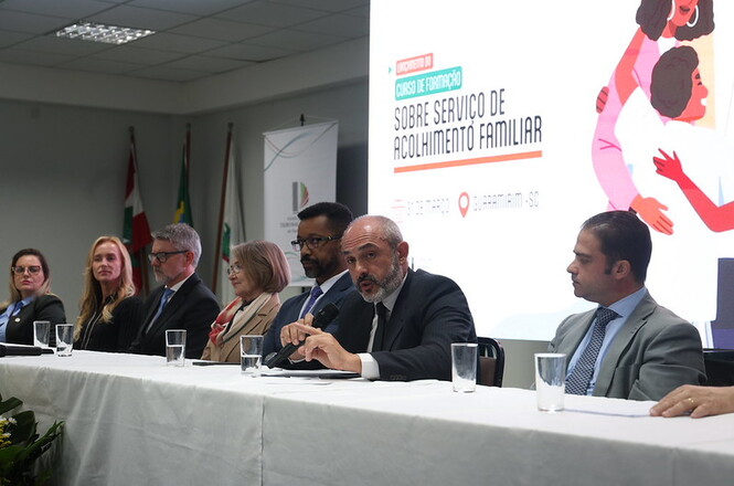 Foto colorida: autoridades sentadas à mesa, plenário institucional interno, curso de formação, debatendo acolhimento familiar