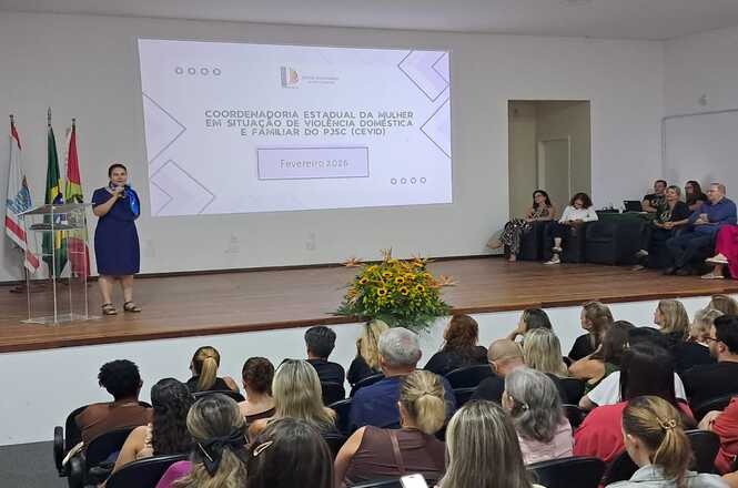 A foto mostra a desembargadora Hildemar Meneguzzi de Carvalho, da Coordenadoria da Mulher em Situação de Violência Doméstica e Familiar (Cevid), do TJSC, palestra ao microfone, enquanto plateia acompanha atenta evento institucional sobre violência doméstica