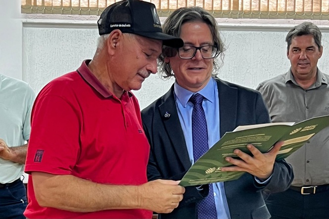 Foto colorida: dois participantes analisando documento, ambiente comunitário interno, ação social, conferindo registros
