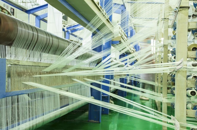 Foto colorida: fios em máquina industrial, fábrica têxtil interna, produção automatizada, tecendo linhas