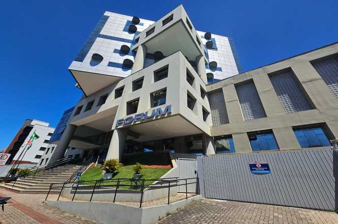 Foto colorida: prédio do fórum em área urbana, fachada institucional, serviço judiciário, destacando arquitetura em azul, branco e cinza