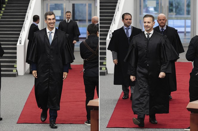 Foto colorida: Silvio Franco e Andreas Eisele, magistrados togados, caminhando sobre tapete vermelho, hall institucional, cerimônia judicial, em preto, cinza e vermelho