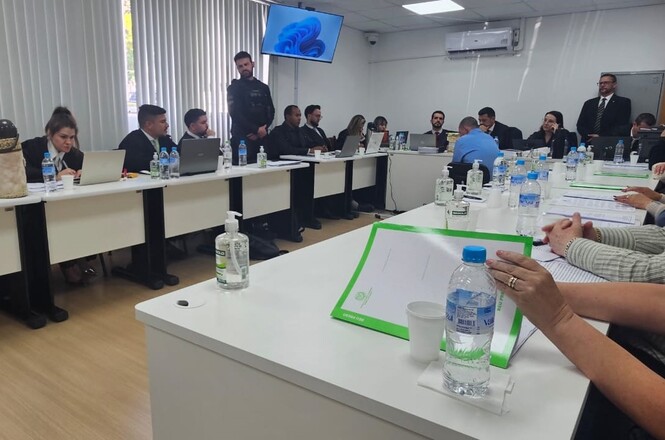 Foto colorida: magistrados e advogados à mesa, sala de audiências, julgamento formal, analisando autos em branco, azul e verde