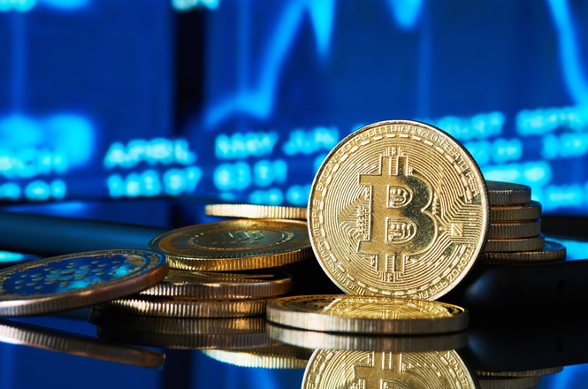 Uma imagem macro de moedas de Bitcoin douradas empilhadas, com um fundo desfocado de gráficos financeiros azuis