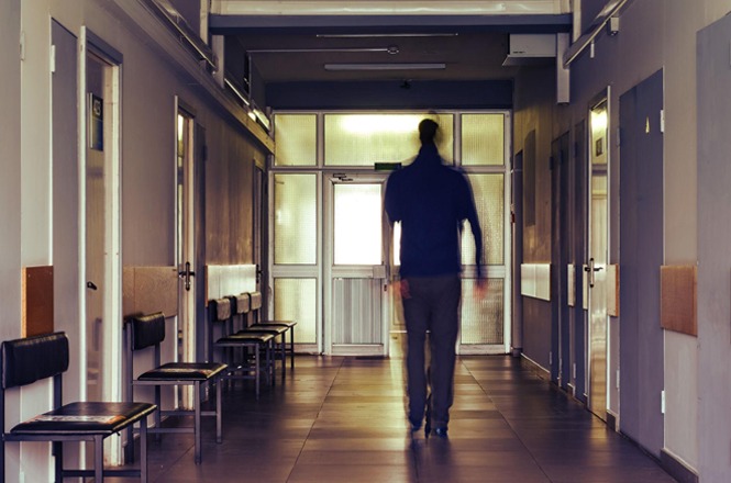 Foto colorida: pessoa caminhando em corredor hospitalar, ambiente interno, atendimento de saúde