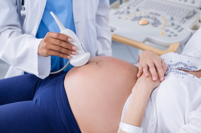 Foto colorida: exame de ultrassom em mulher grávida, consultório clínico interno, cuidado pré-natal, realizando avaliação