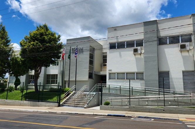 Foto colorida: prédio do fórum com fachada moderna, área urbana externa, sede judiciária, destacando acesso em branco, cinza e verde