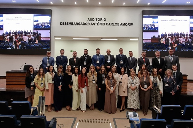 Foto colorida: grupo posando em auditório do TJSC, ambiente institucional interno, encontro estadual, registrando participação em bege, preto e azul