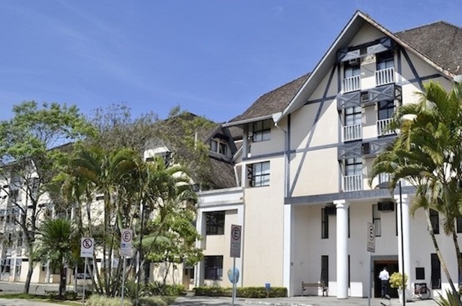 Foto colorida: prédio institucional de estilo europeu, área urbana arborizada, sede pública, destacando arquitetura em bege, branco e verde