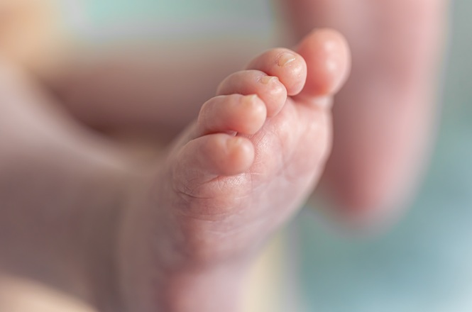 Foto colorida: pé de bebê em close, ambiente interno suave, cuidado infantil, exibindo detalhe delicado em tons rosa, bege e azul claro