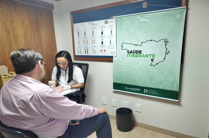 Foto colorida: profissional coletando material em paciente, consultório interno, saúde itinerante, realizando exame em verde, branco e bege