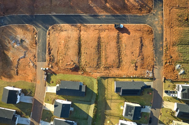 Foto colorida: loteamento visto de cima com casas e ruas, área urbana em expansão, desenvolvimento imobiliário, organizando terrenos em marrom, verde e cinza