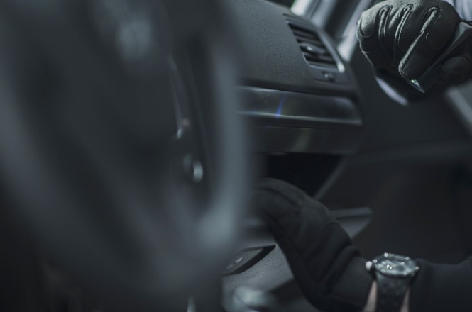 Foto colorida: mãos com luvas no interior de veículo, ambiente automotivo fechado, procedimento técnico, inspecionando painel em preto e cinza