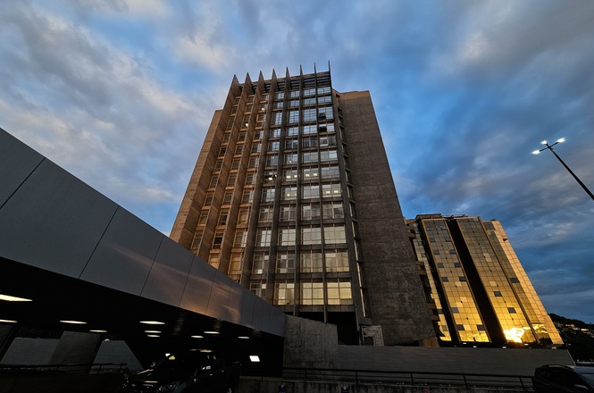 Foto horizontal: prédio do TJSC se destaca sob céu nublado ao entardecer em tons azul e dourado.
