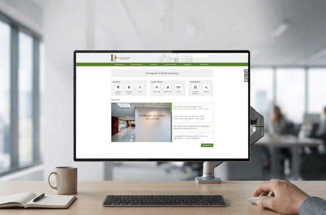 Foto horizontal: monitor exibe portal da Corregedoria-Geral de Justiça em mesa de trabalho, ambiente de escritório, tons neutros.