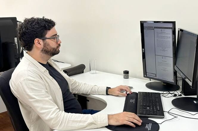 Foto pessoa em preto e branco no escritório bege, ambiente corporativo, digitando no computador