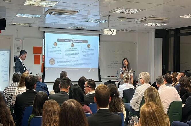 Foto horizontal: palestrantes conduzem capacitação jurídica com público em sala de treinamento iluminada.