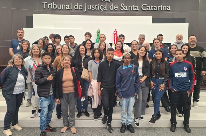 Foto horizontal: grupo de pessoas posa no plenário do TJSC, adultos e jovens reunidos em escadaria, ambiente institucional, clima coletivo.