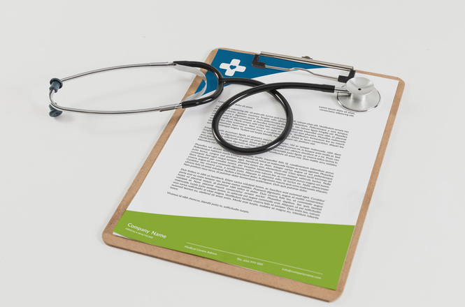 Foto horizontal: estetoscópio sobre prancheta com documento médico, símbolo da área da saúde, fundo claro, tons neutros.