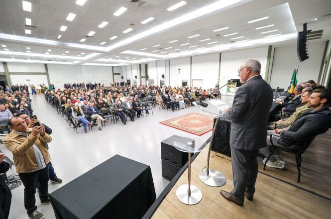 Foto horizontal: autoridade discursa em púlpito diante de grande público em auditório, plateia atenta, ambiente institucional, clima solene.
