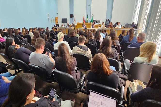 Foto horizontal: auditório com público numeroso acompanha mesa de autoridades ao fundo, evento institucional em andamento, ambiente formal, clima de participação e debate.