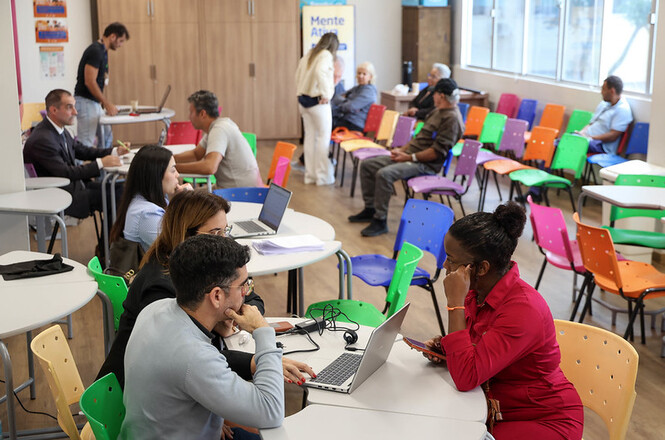 Foto horizontal: atendimento em espaço comunitário com equipe e usuários, clima de orientação e acolhimento.