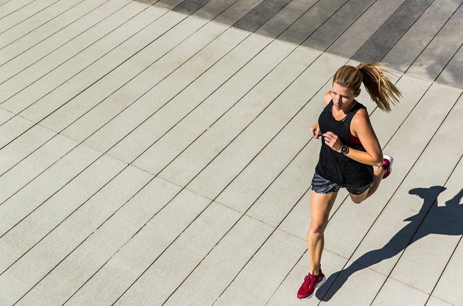 Foto horizontal: mulher corre em área urbana ao ar livre, movimento em destaque, clima de saúde e atividade física.