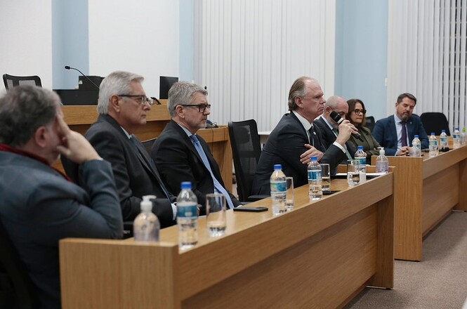 Foto horizontal: o desembargador Rubens Schulz fala ao microfone em mesa de autoridades, participantes ao lado acompanham, ambiente institucional, clima de debate e articulação.