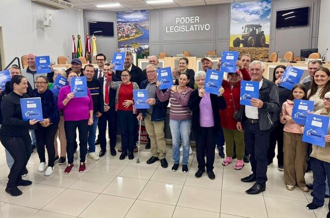 Foto horizontal: grupo posa no Poder Legislativo com documentos em mãos, registro coletivo, clima de conquista e inclusão social.