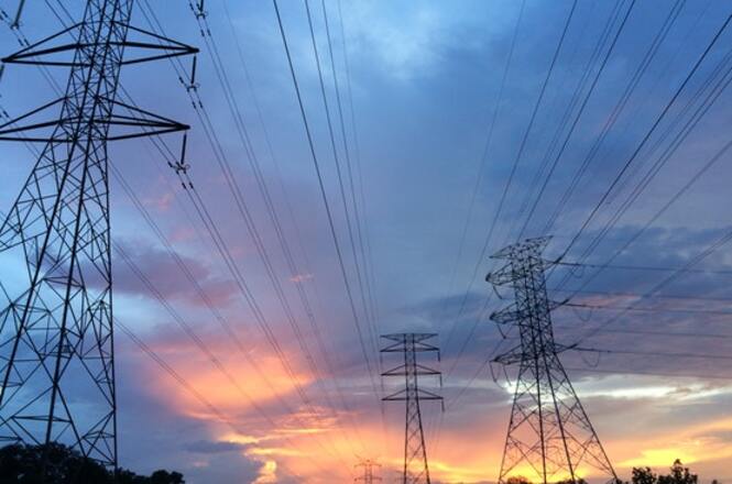 Foto horizontal: torres de transmissão de energia sob céu ao entardecer, linhas elétricas em destaque, clima de infraestrutura e desenvolvimento.