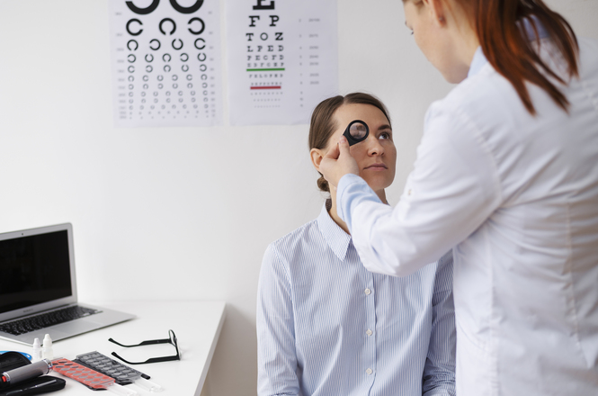 Foto horizontal: profissional de saúde realiza exame ocular em paciente, ambiente clínico, clima de cuidado e avaliação visual.