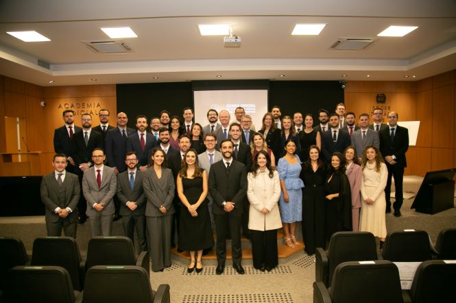 Foto horizontal: grupo posa em solenidade de formatura na Academia Judicial, participantes alinhados em ambiente institucional, clima de celebração e conquista profissional.