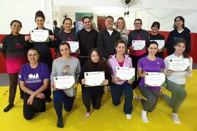 Foto horizontal: grupo de mulheres exibe certificados em atividade institucional, ambiente coletivo, clima de conquista, valorização e fortalecimento feminino.