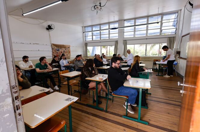 Foto horizontal: candidatos realizam prova em sala de aula, ambiente organizado, clima de concentração e avaliação para ingresso na magistratura.