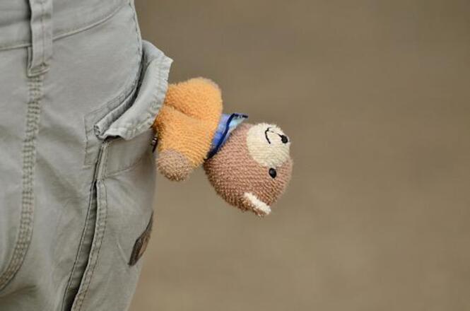 Foto horizontal: boneco de pelúcia aparece parcialmente em bolso de calça, detalhe lúdico, clima de infância e delicadeza.