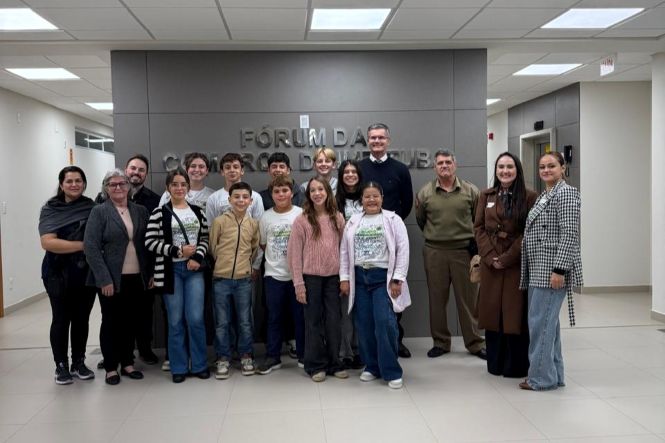 Foto horizontal: grupo de estudantes e autoridades posa no Fórum de Imbituba, visita institucional em destaque, clima de educação cidadã e integração comunitária.