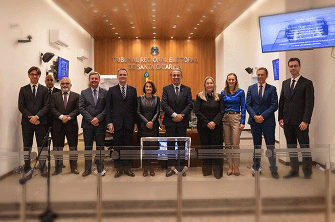 Foto horizontal: autoridades posam em solenidade no Tribunal Regional Eleitoral de Santa Catarina, grupo alinhado em ambiente institucional, clima de formalidade e cooperação institucional.