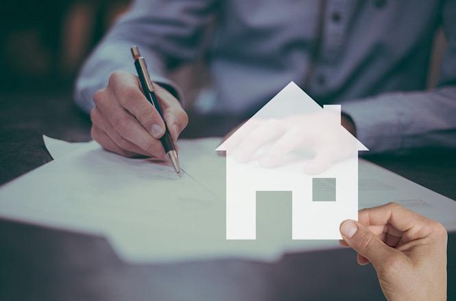 Foto horizontal: pessoa assina documento com ícone de casa em destaque, simbolizando contrato imobiliário, clima de negociação e aquisição de patrimônio.