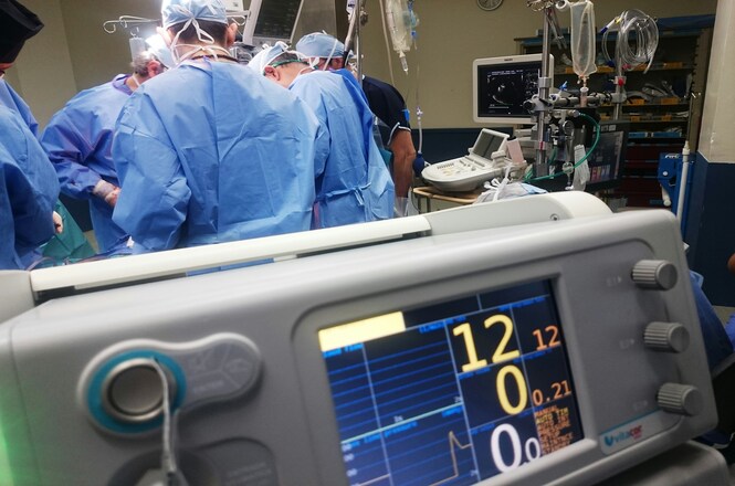 Equipe médica realiza procedimento cirúrgico em hospital, com monitoramento em destaque, clima de precisão e cuidado com a vida