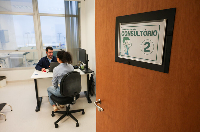 Foto horizontal: atendimento ocorre em consultório do Programa Novos Caminhos, com profissional e paciente sentados diante de mesa de trabalho.