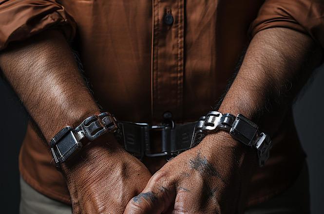 Foto horizontal: mãos algemadas em primeiro plano simbolizam prisão, detenção ou cumprimento de medida judicial.