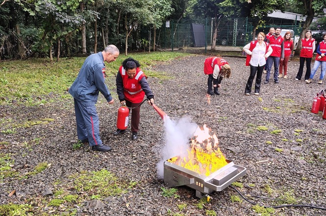 Foto horizontal: participantes realizam treinamento de combate a incêndio, utilizando extintores em atividade prática ao ar livre.