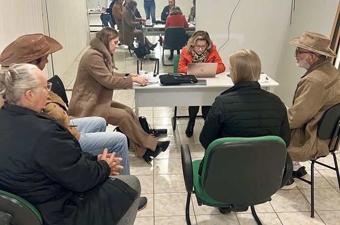 Foto horizontal: cidadãos recebem atendimento individualizado em mutirão de regularização fundiária, com equipes realizando análise e orientação documental.